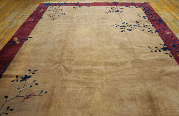Tan, high-sheen rug featuring a wide burgundy border and blue floral vine patterns on wood planks.