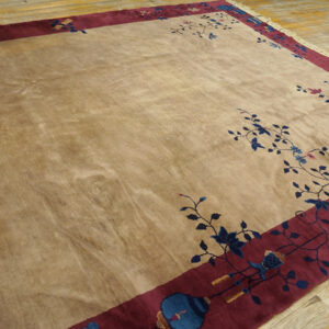 A lustrous beige rug with blue floral vines and a wide burgundy border rests on a wooden floor.