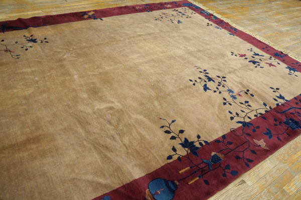 A lustrous beige rug with blue floral vines and a wide burgundy border rests on a wooden floor.