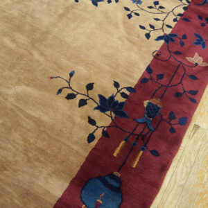 Plush tan rug detail showing a burgundy border and navy floral patterns, next to blonde hardwood flooring.