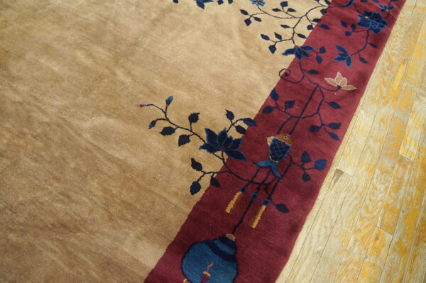 Plush tan rug detail showing a burgundy border and navy floral patterns, next to blonde hardwood flooring.