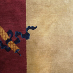 Maroon rug field with gold checkered scrolls and navy ribbons bordered by solid tan pile.
