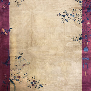 A lustrous beige rug features a wide magenta border detailed with stylized blue floral and bird motifs.