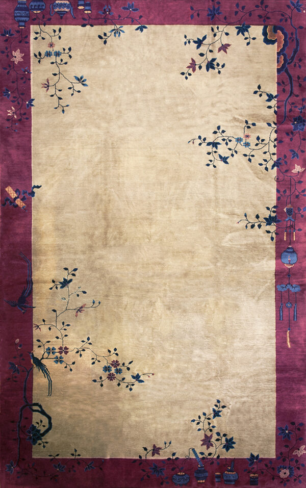A lustrous beige rug features a wide magenta border detailed with stylized blue floral and bird motifs.