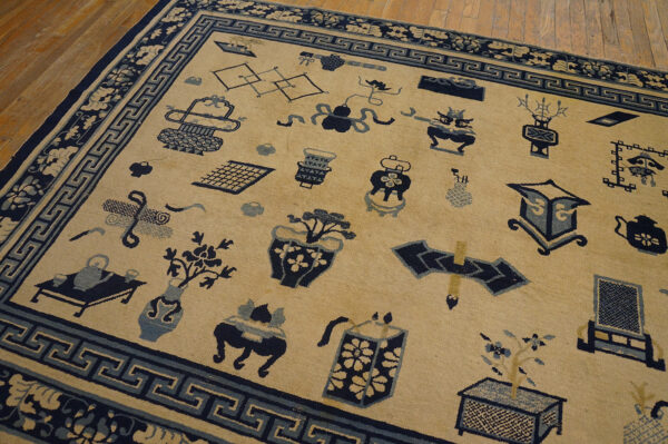 A tan rug with navy blue objects and geometric borders rests on light brown wooden floorboards.