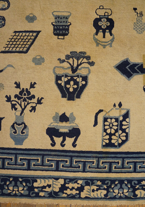 Cream field rug with scattered navy and light blue artifact motifs and a prominent greek key border.