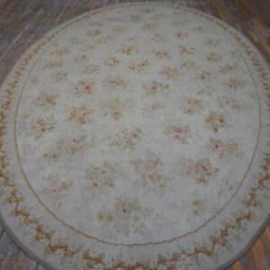 Oval cream rug with a pink and tan floral pattern, including a detailed border, resting on wood planks.