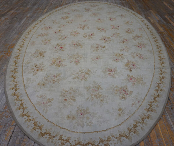 Oval cream rug with a pink and tan floral pattern, including a detailed border, resting on wood planks.