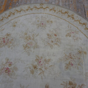 Low-pile oval rug featuring soft pink and beige floral motifs on a pale ground over wood floors.