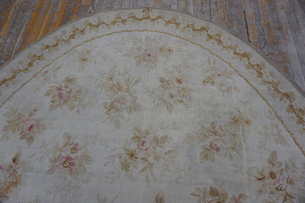 Low-pile oval rug featuring soft pink and beige floral motifs on a pale ground over wood floors.