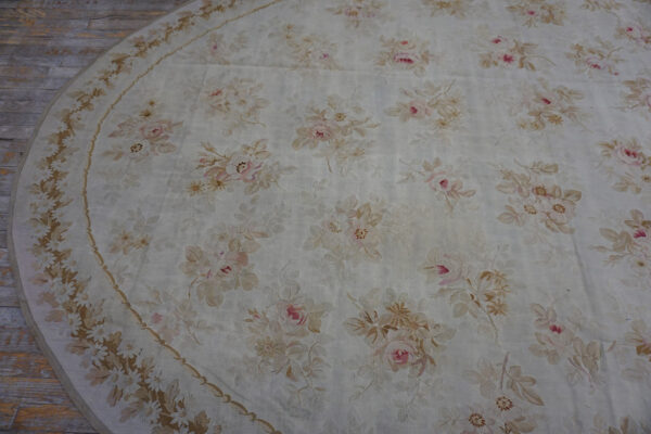 Oval cream rug featuring a faded floral pattern of blush pink and beige roses on light wood flooring.