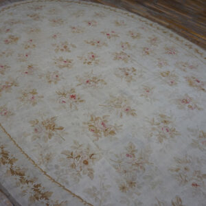 Oval cream rug with an all-over low-pile floral pattern in pink, tan, and beige on wood flooring.