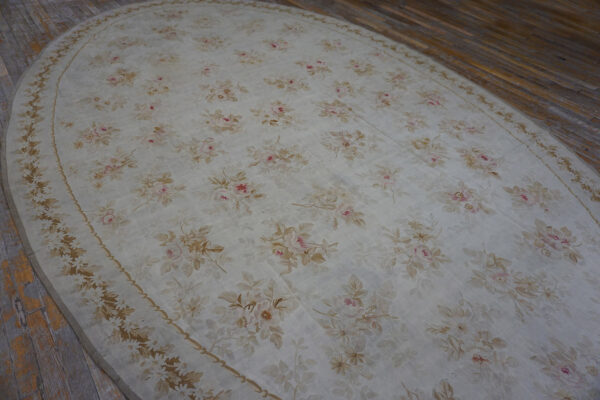 Oval cream rug with an all-over low-pile floral pattern in pink, tan, and beige on wood flooring.