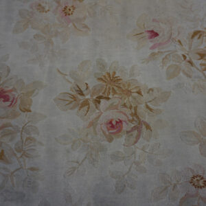 Close view of a low-pile oval rug with all-over beige and pink floral design on a cream ground.