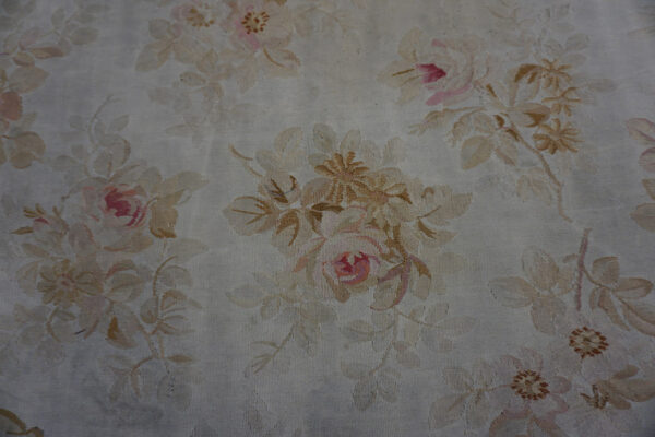 Close view of a low-pile oval rug with all-over beige and pink floral design on a cream ground.