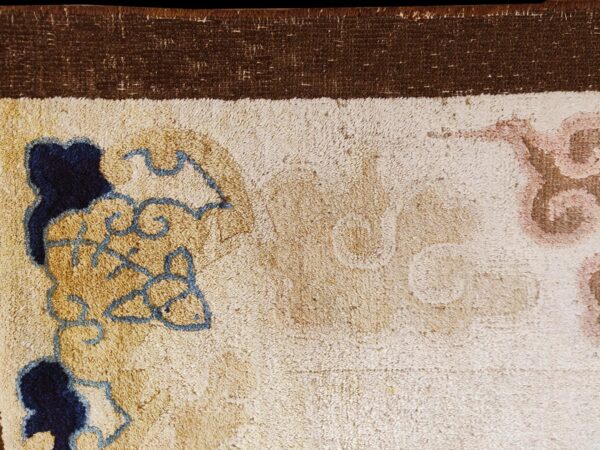 High-pile rug detail showing a dark brown border and field with blue, gold, and muted pink scroll patterns.