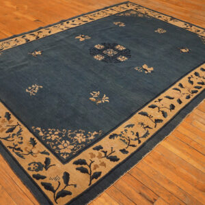 Low-pile deep blue rug with a wide tan floral border rests on golden hardwood floors.