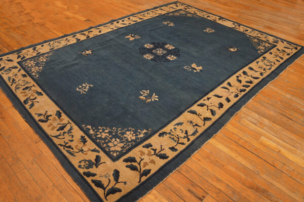 Low-pile deep blue rug with a wide tan floral border rests on golden hardwood floors.