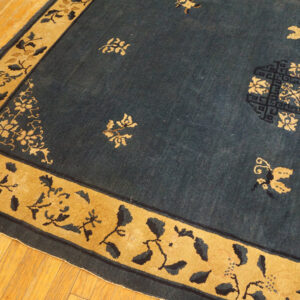 Low-pile indigo rug with gold border and stylized floral and butterfly patterns on hardwood.