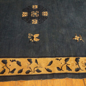 Deep blue rug with scattered tan floral motifs, a circular medallion, and a wide stylized gold border on wood floor.