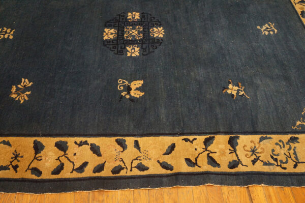 Deep blue rug with scattered tan floral motifs, a circular medallion, and a wide stylized gold border on wood floor.