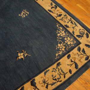 Blue rug with tan border and botanical patterns rests on polished hardwood planks.
