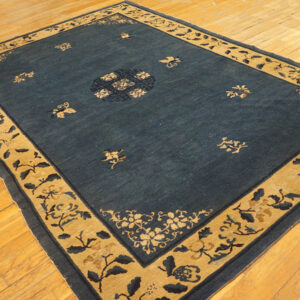 Deep blue rug with a wide gold border and floral patterns rests on light hardwood floors.