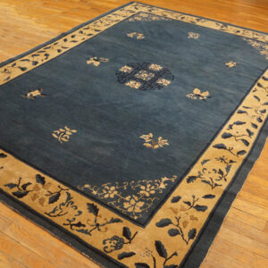 Dark blue rug with a wide tan border and floral patterns lies on varnished hardwood flooring.