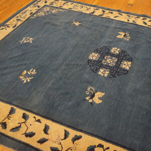 Blue rug with scattered tan floral designs and a wide tan border on a wooden floor.