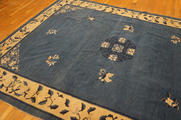 Blue rug with scattered tan floral designs and a wide tan border on a wooden floor.