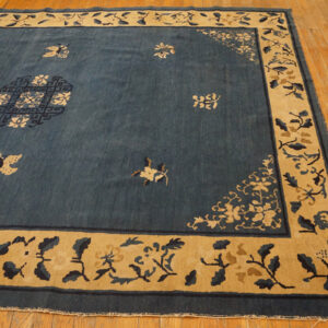 Deep indigo rug with a wide tan and dark blue floral border laid over a wood floor.