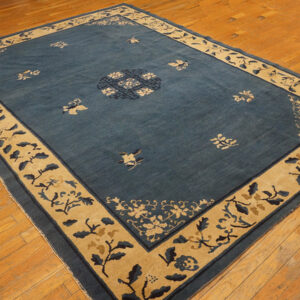 A large blue rug with a wide tan botanical border and scattered floral motifs rests on wood plank flooring.