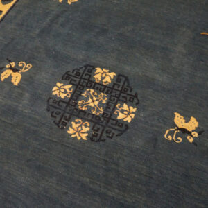 Detail view of a blue rug with beige motifs, a wide geometric border, and a central circular medallion.