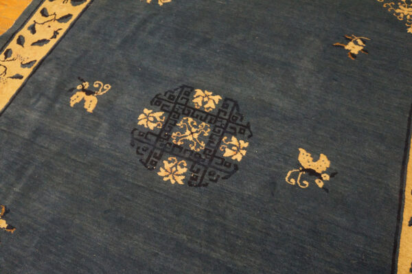 Detail view of a blue rug with beige motifs, a wide geometric border, and a central circular medallion.