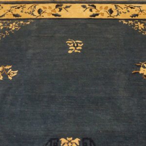 Dark blue low-pile rug featuring a wide tan border with intricate floral spandrel and central motifs on wood flooring.