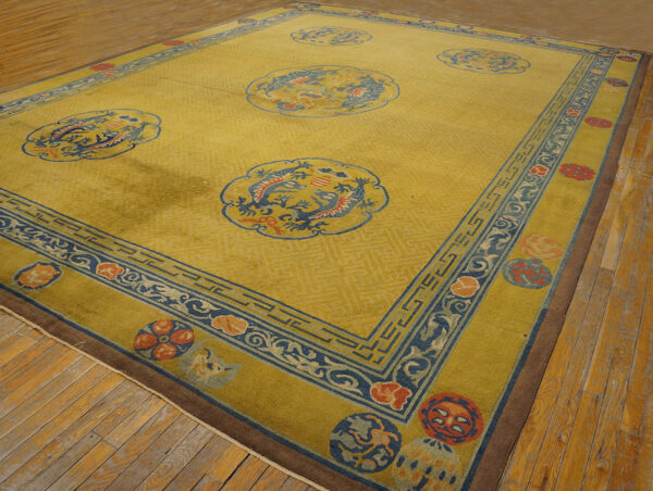 Gold rug with blue and red dragon medallions and geometric borders rests on worn wooden flooring.