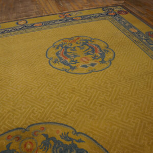 Yellow area rug featuring tonal fretwork, blue medallions, and a complex border on wood plank flooring.