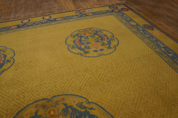 Yellow area rug featuring tonal fretwork, blue medallions, and a complex border on wood plank flooring.