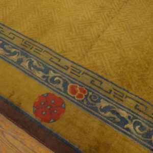 Golden yellow high-pile rug featuring blue fretwork and red floral medallions on a complex border, resting on wood floor.