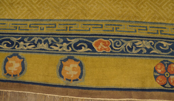 Gold and blue rug detail showing fretwork, scrolling vines, and orange medallions over wood floor.