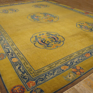 Gold-yellow area rug with five blue dragon medallions and a wide blue and orange ornamental border on wood flooring.
