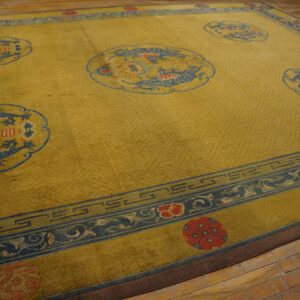 Golden yellow rug with tone-on-tone fretwork, large blue dragon medallions, and blue floral borders on wood flooring.
