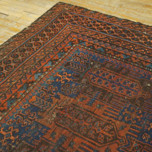 Close-up showing the geometric border of a deep rust and dark blue rug on light wooden flooring.