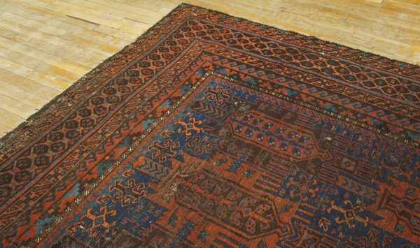 Close-up showing the geometric border of a deep rust and dark blue rug on light wooden flooring.