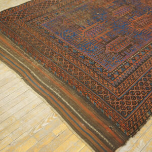 Low-pile rug with complex blue and rust geometric patterns and striped ends lying on pale wood flooring.
