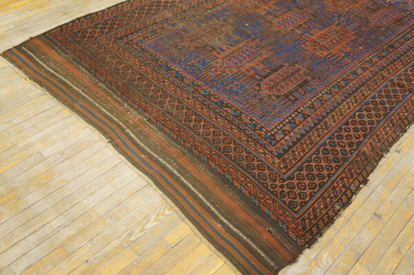Low-pile rug with complex blue and rust geometric patterns and striped ends lying on pale wood flooring.