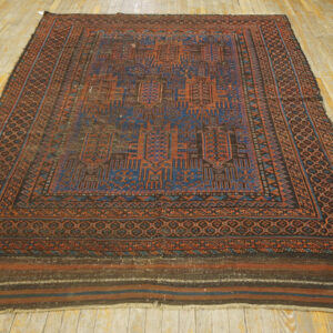 Geometric rug featuring deep blue and rust motifs, bordered in brown, covers a worn wood floor.