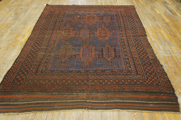 Geometric rug featuring deep blue and rust motifs, bordered in brown, covers a worn wood floor.