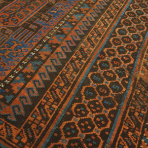 Geometric patterned rug featuring blue, orange, and dark brown motifs resting on light wood flooring.