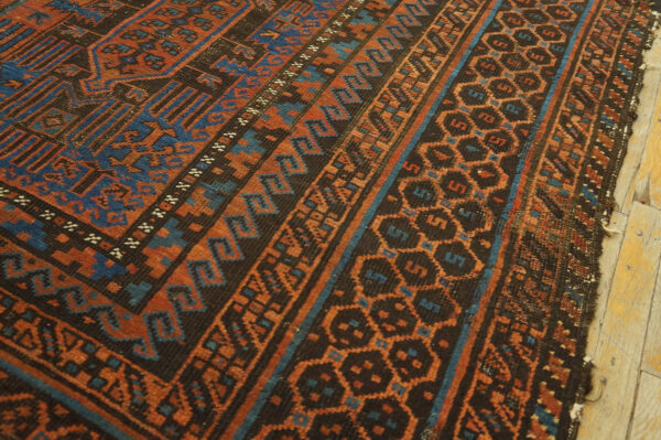 Geometric patterned rug featuring blue, orange, and dark brown motifs resting on light wood flooring.